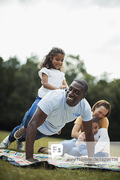 Verspielter Vater macht Push-ups mit der Tochter auf dem Rücken im Park