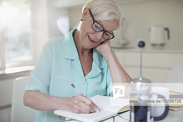 Ältere Frau schreibt in der Morgenküche im Journal