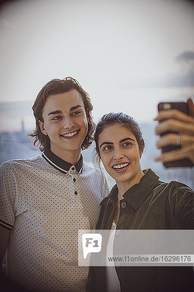 Glückliches junges Paar  das sich mit einem Fotohandy am Fenster selbstständig macht