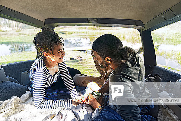 Glückliches  liebevolles junges Paar entspannt sich auf einer Autoreise hinten im Auto