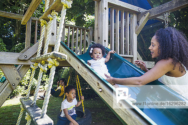 Mutter beobachtet süße Kleinkind-Tochter auf Spielplatzrutsche im Hinterhof
