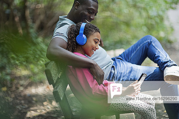 Vater und Tochter mit Kopfhörer und digitalem Tablett auf der Parkbank