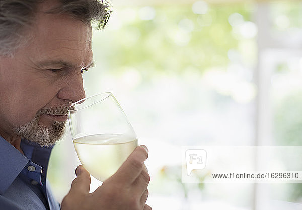 Nahaufnahme eines älteren Mannes der Weißwein riecht und schmeckt