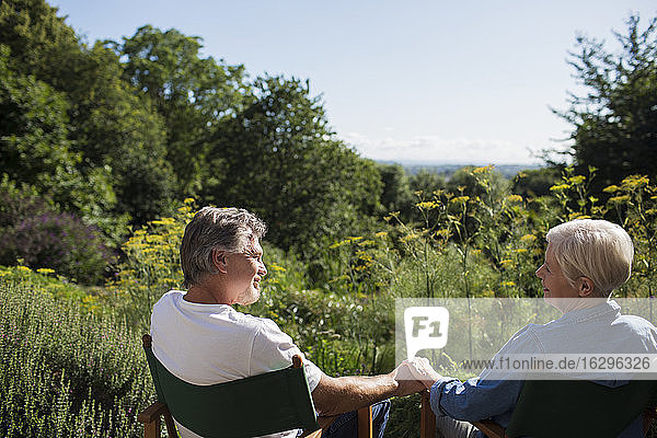 Liebenswertes älteres Ehepaar hält im sonnigen Sommergarten Händchen