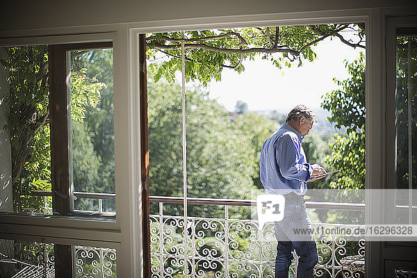 Älterer Mann benutzt digitales Tablet auf sonnigen idyllischen Balkon