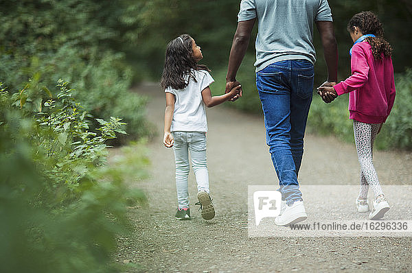 Vater und Töchter halten sich beim Spaziergang im Park an den Händen