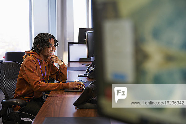 Lächelnder junger Geschäftsmann arbeitet am Computer im Büro