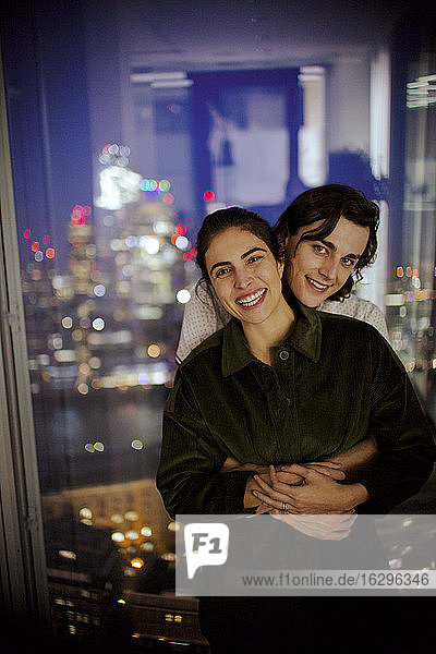 Porträt eines glücklichen jungen Paares  das sich am Hochhausfenster umarmt