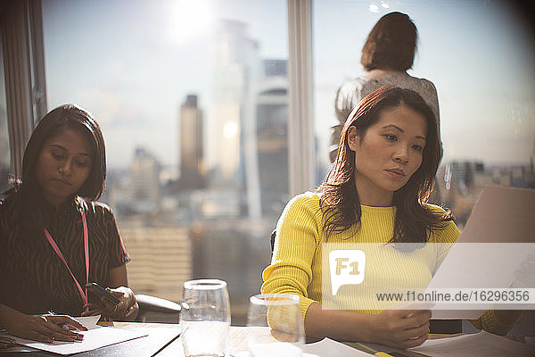 Businesswomen reviewing paperwork in highrise conference room meeting