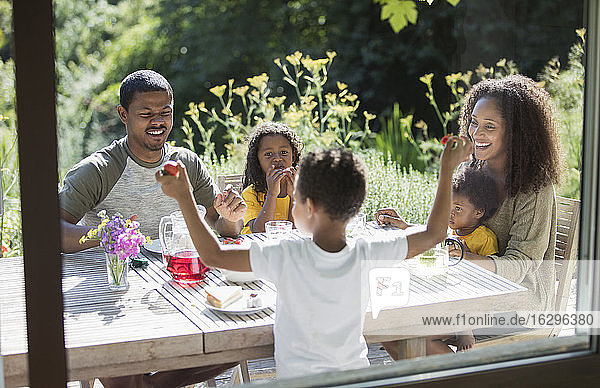 Glückliche Familie genießt das Mittagessen im Garten auf der sonnigen Sommerterrasse
