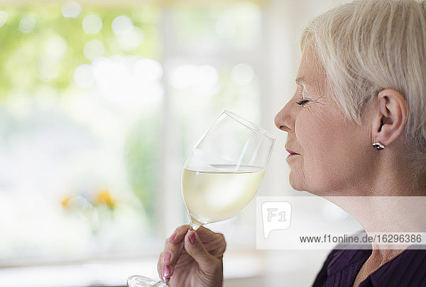 Gelassene ältere Frau riecht und schmeckt Weißwein