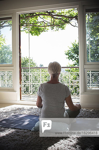 Ruhige ältere Frau meditiert an ruhiger Balkontür im Sommer