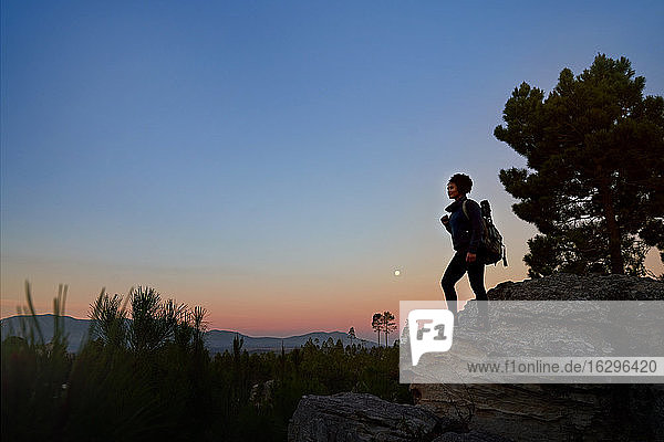 Junge Wanderin auf Fels in landschaftlich ruhiger Wüste in der Abenddämmerung