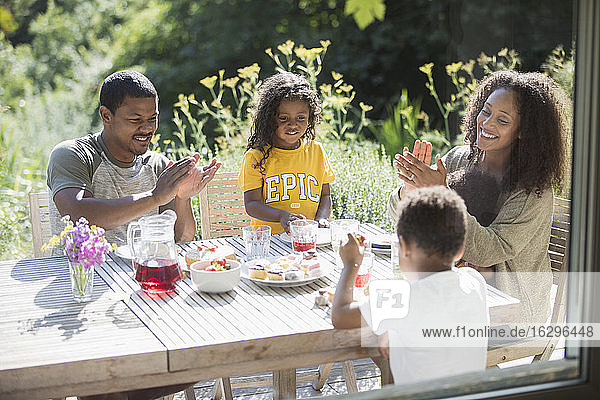 Glückliche Familie klatscht und isst am sonnigen Sommerterrassentisch