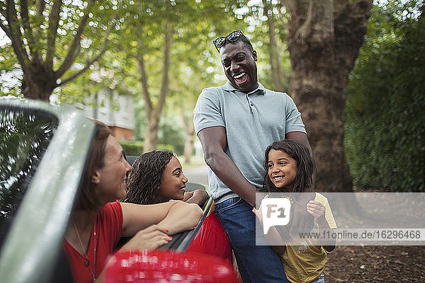 Happy family laughing at convertible in driveway
