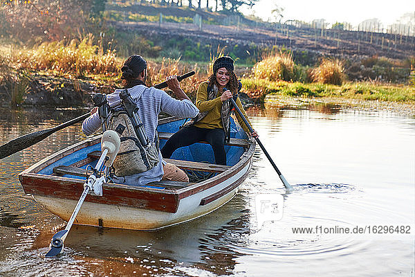 Glückliches junges Paar mit Rudern im Ruderboot auf sonnigem Herbstsee