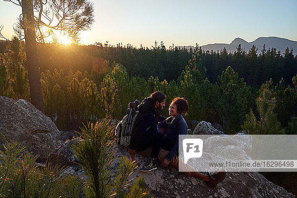 Happy affectionate young couple relaxing on rocks in woods at sunset