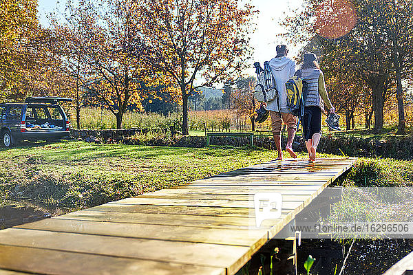 Barfüßiges junges Paar beim Spaziergang am sonnigen Herbstufer des Sees