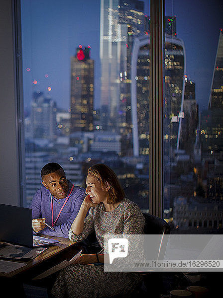 Business people working late at laptop in highrise office  London  UK