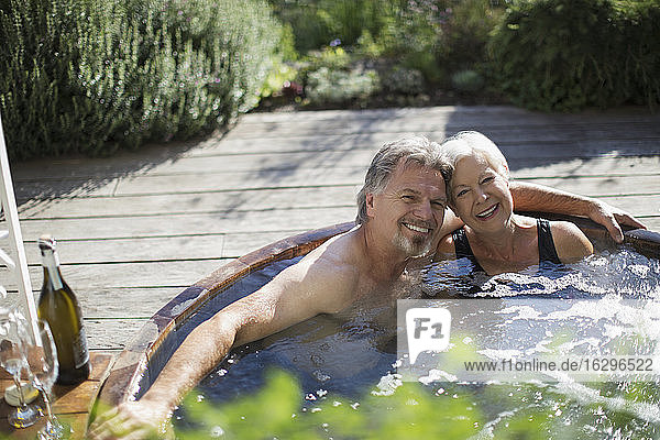 Porträt eines glücklichen älteren Paares  das sich im Whirlpool auf der sonnigen Terrasse entspannt