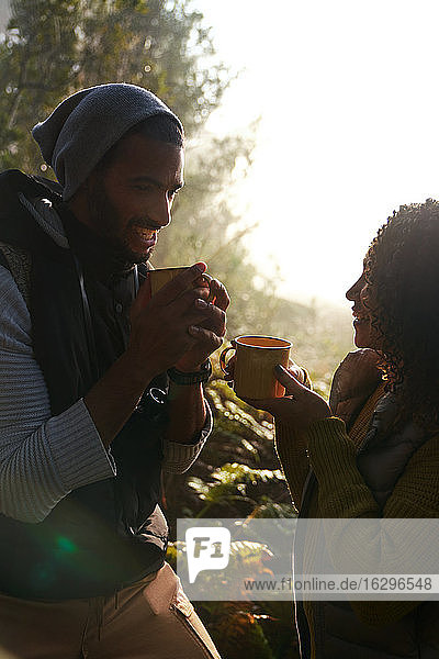 Glückliches junges Wandererpaar trinkt Kaffee in sonnigen Wäldern