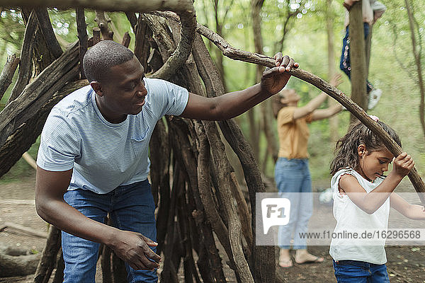 Father and daughter building fort with tree branches in woods