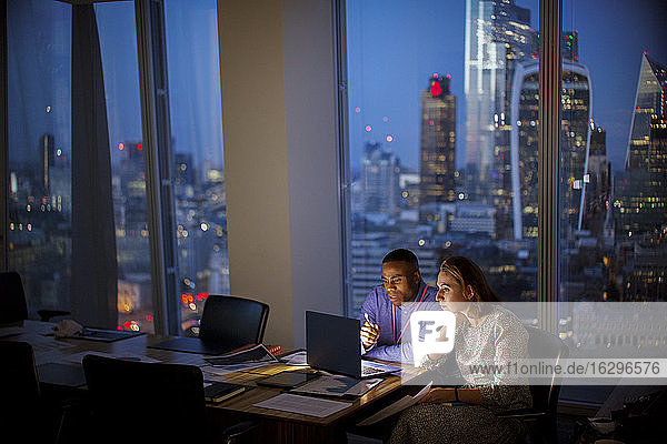 Business people working late at laptop in highrise office  London  UK