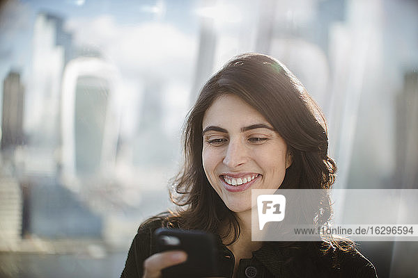 Smiling businesswoman using smart phone in sunny window
