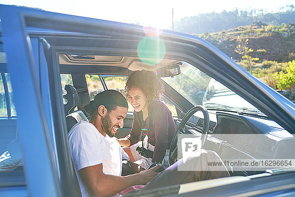 Happy young couple laughing on road trip in sunny car