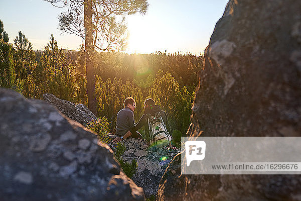 Affectionate young hiker couple relaxing on rock in sunny sunset woods