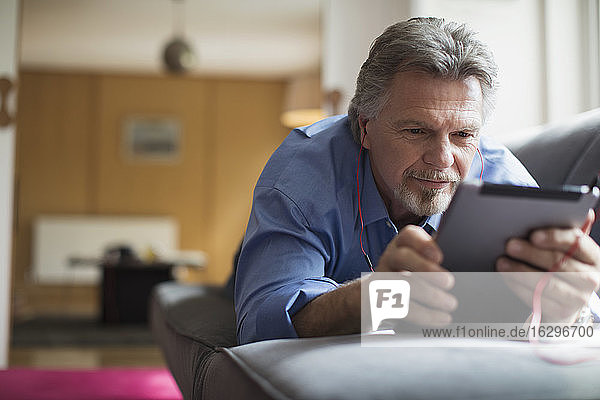 Älterer Mann benutzt Kopfhörer und digitales Tablet auf Wohnzimmersofa
