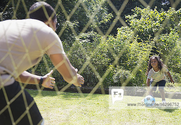 Father and daughter playing soccer in sunny summer backyard