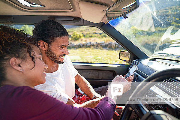 Young couple using smart phone on road trip in sunny car