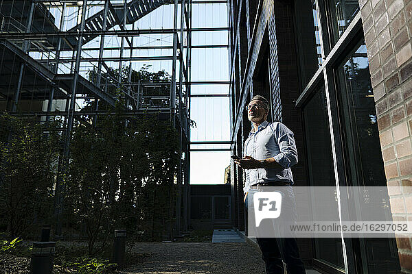Männlicher Unternehmer  der ein Smartphone benutzt  während er vor einem Bürogebäude steht