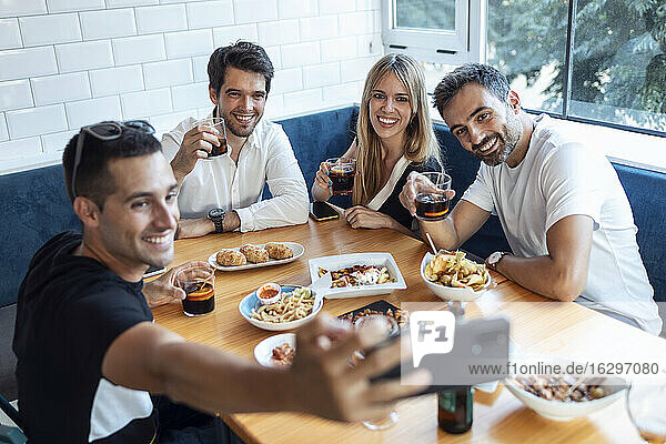 Group of friends taking selfie while having meal at restaurant
