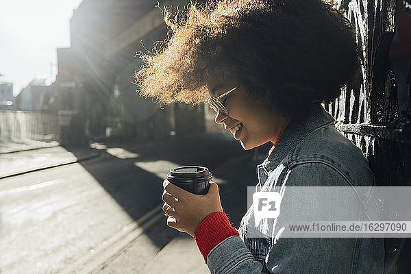 Nahaufnahme einer lächelnden Afro-Frau  die an einem sonnigen Tag einen Einwegbecher auf der Straße hält