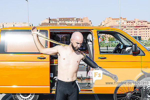 Kahlköpfiger Anpassungssportler  der eine Handprothese trägt  während er gegen einen Lieferwagen steht