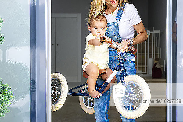 Mutter spielt mit ihrem Sohn auf dem Dreirad sitzend zu Hause