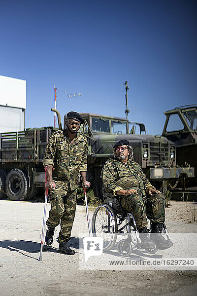 Verletzter Militäroffizier  der Krücken hält  während er mit einem behinderten Armeesoldaten im Rollstuhl an einem sonnigen Tag steht