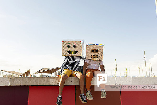 Freunde in Roboterkostümen sitzen im Sommer auf einer Stützmauer gegen den klaren Himmel