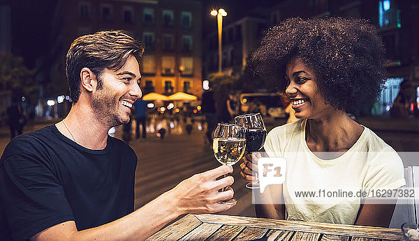 Fröhliches Paar  das sich anschaut  während es mit Weingläsern auf einen gemeinsamen Abend anstößt