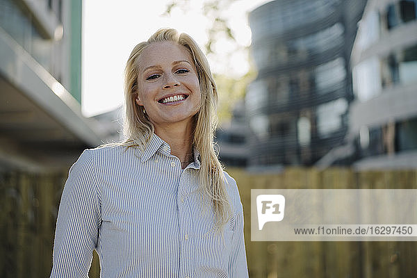 Lächelnde blonde Unternehmerin in Geschäftskleidung im Finanzviertel