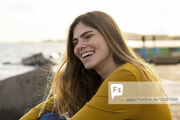 Cheerful young woman sitting by sea against sky