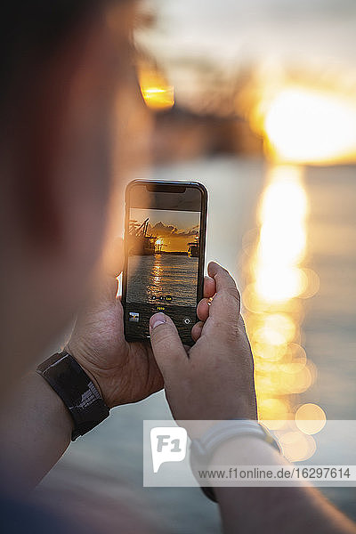 Deutschland  Hamburg  Hände eines Mannes  der mit seinem Smartphone Fotos vom Hamburger Hafen bei Sonnenuntergang macht