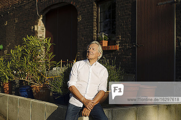 Nachdenklicher Mann mit geschlossenen Augen  der auf einer Stützmauer im Hof sitzt