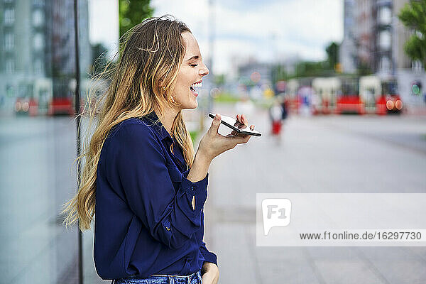 Frau lacht  während sie den Lautsprecher ihres Smartphones in der Stadt benutzt
