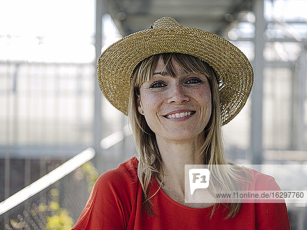 Nahaufnahme einer lächelnden Geschäftsfrau mit Hut im Gewächshaus