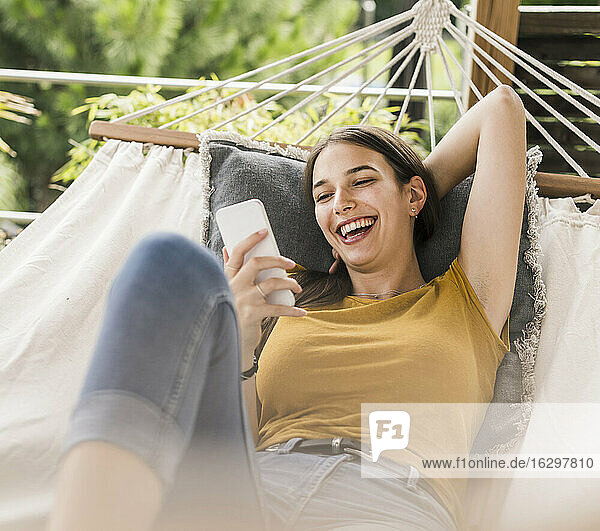 Cheerful beautiful woman using mobile phone while resting on hammock