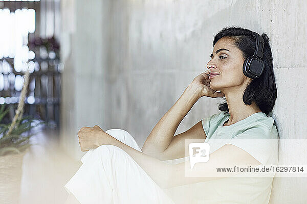 Nachdenkliche Unternehmerin hört Musik über Kopfhörer  während sie im Büro an der Wand sitzt