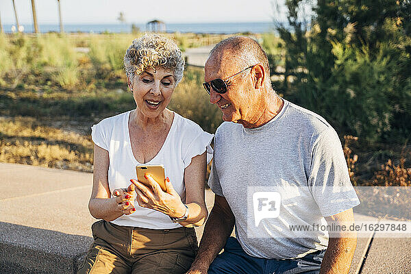 Älterer Mann und Frau telefonieren im Park sitzend